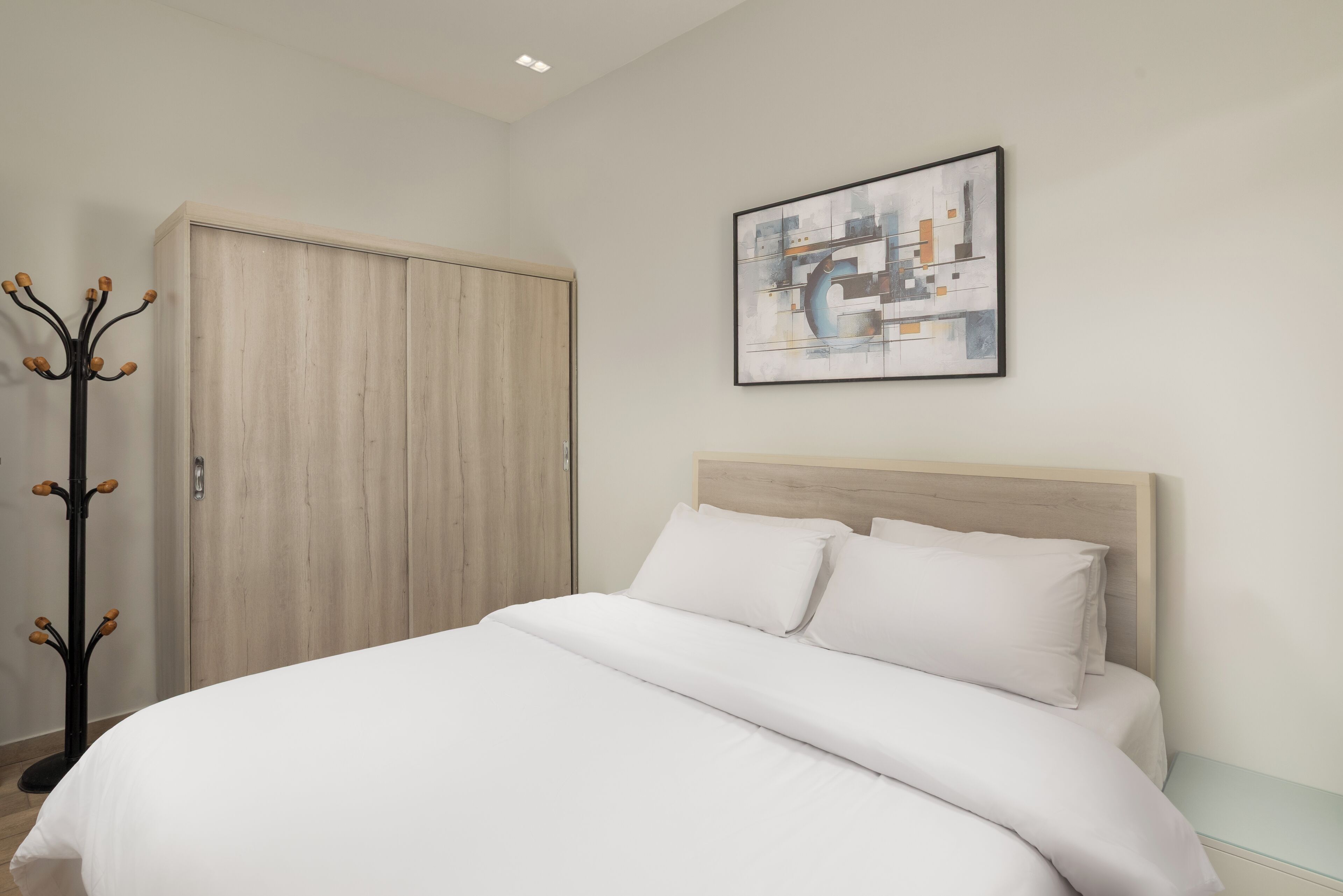 A bedroom with a bed, a coat rack, and a wall-mounted abstract painting.