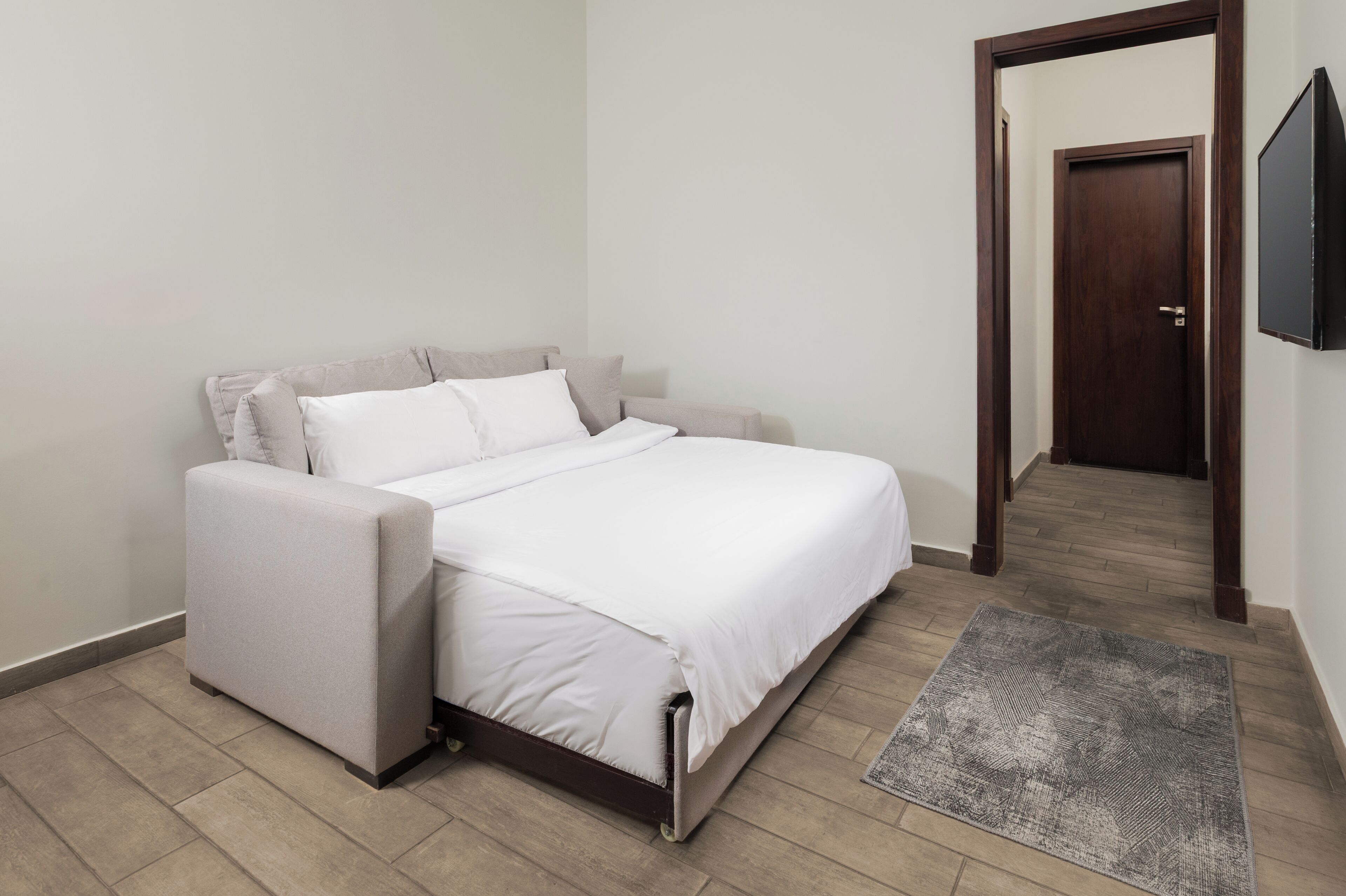 Een slaapkamer met een bed, een stoel, een vloerkleed en een deur naar een andere kamer.