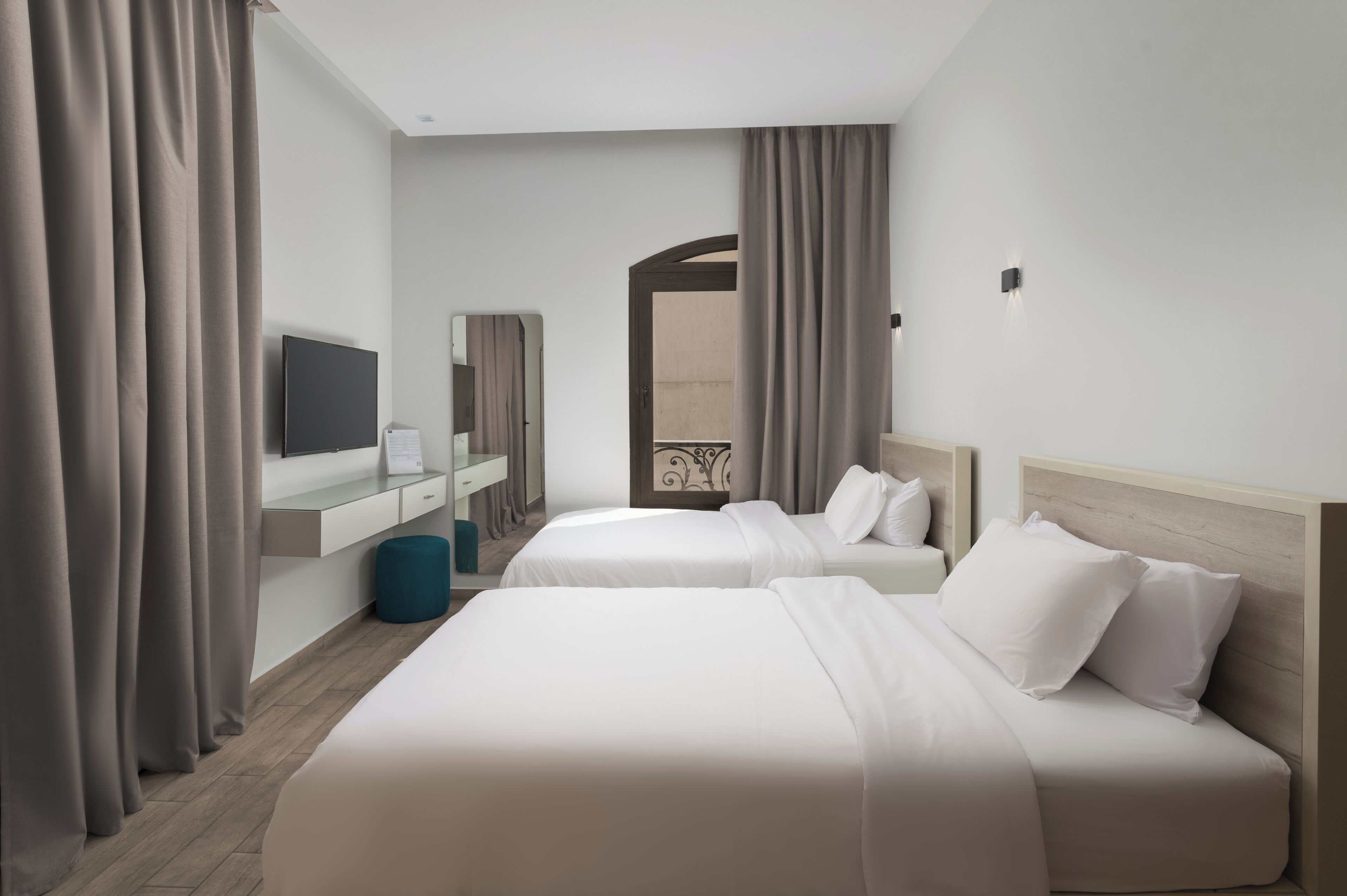 A hotel room with two beds, a TV, a mirror, and a window with curtains.