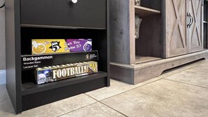 A black shelf with a white knob, displaying items like a wooden piano, a football betting book, and a canister. - Katy Hideaway Charming 3 Bdr! (Katy)