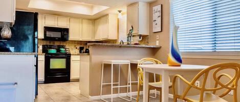A kitchen with white cabinets, a black refrigerator, a microwave, and a stove. There is a dining table with two chairs and a vase on the counter.