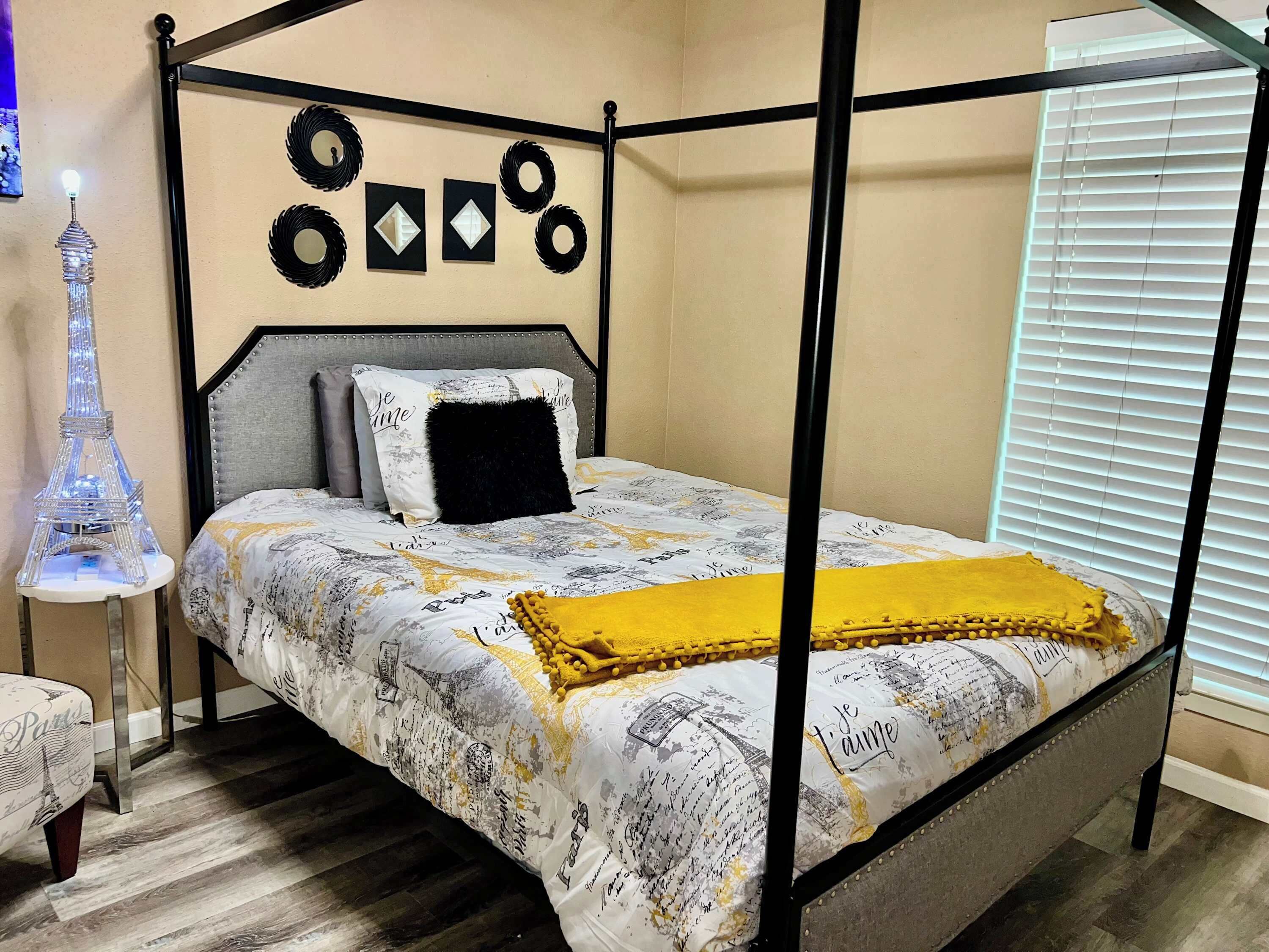 Un lit à baldaquin avec une couvre-lit à motifs, un plaid noir et des œuvres d’art décoratives accrochées au mur.