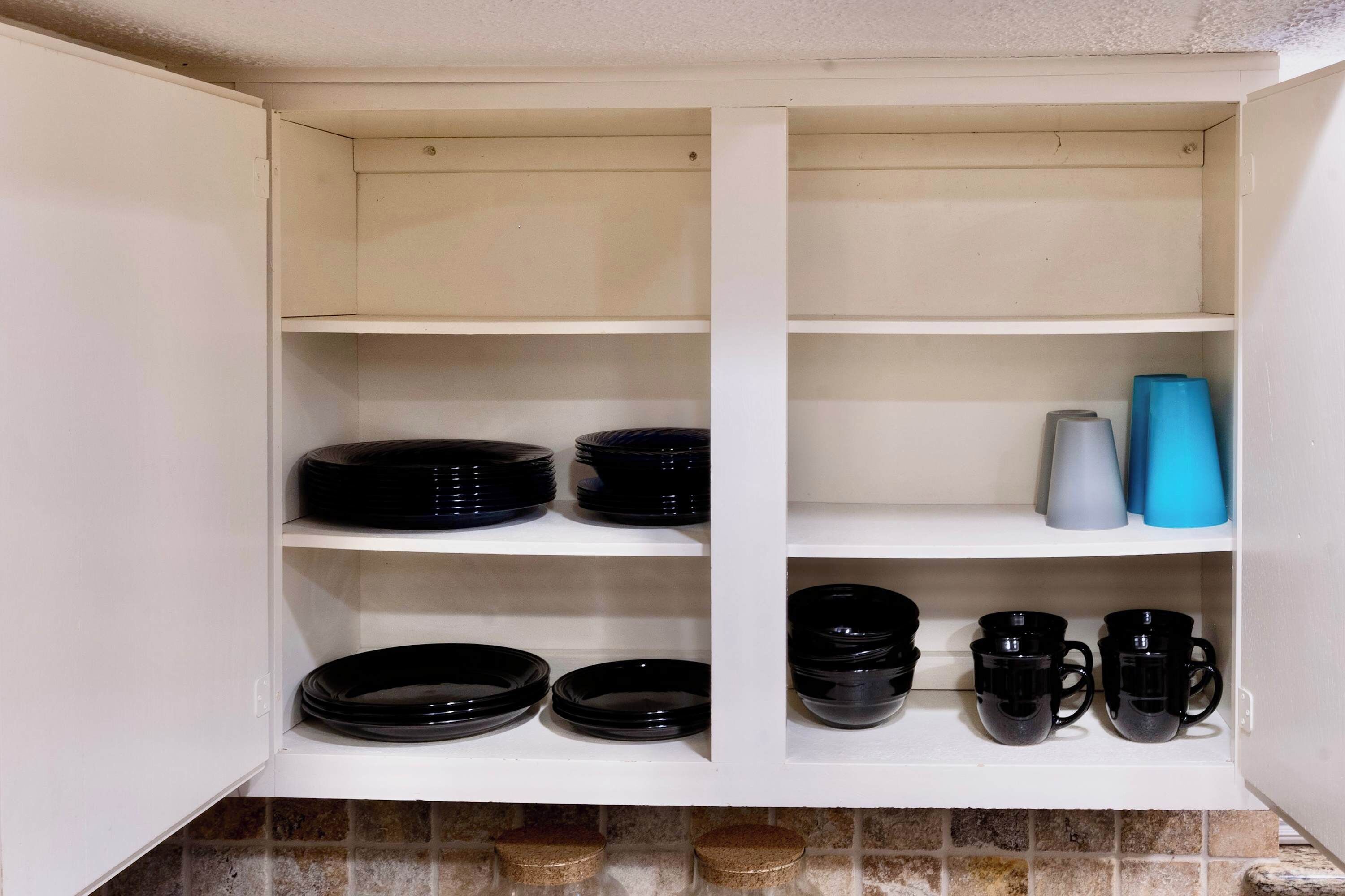 Un meuble de cuisine avec des étagères où sont rangées des assiettes noires, des bols et des tasses noires.