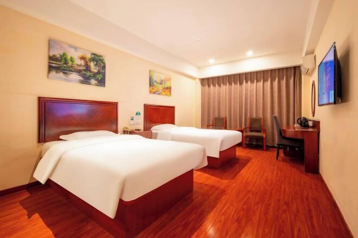A hotel room with two beds, a desk, a chair, a TV, and artwork on the walls.