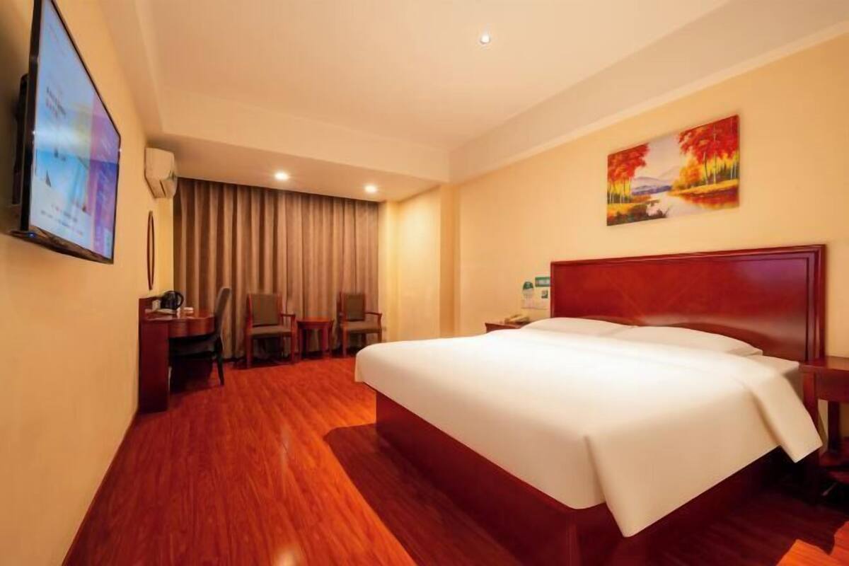 A hotel room with a large bed, a desk with a chair, a television, and a painting on the wall.
