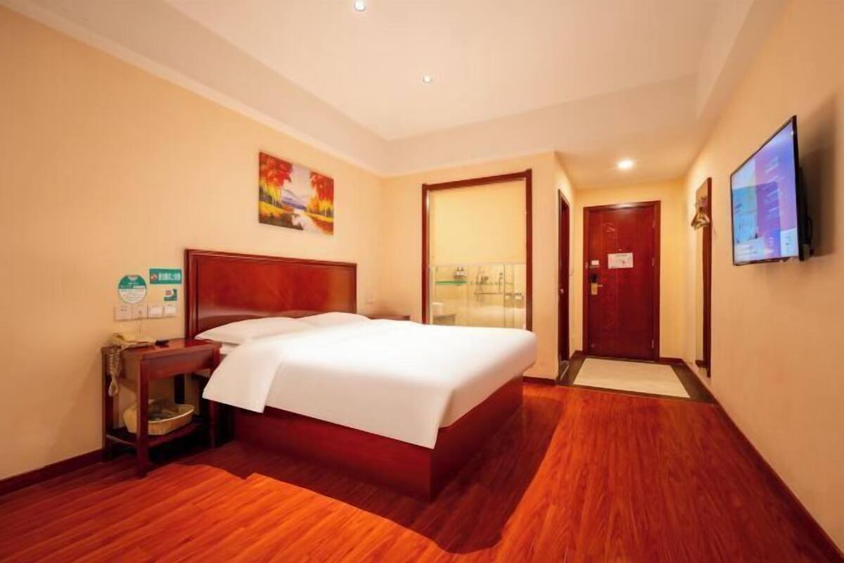 A hotel room with a large bed, a wooden floor, a flat-screen TV, and a painting on the wall.