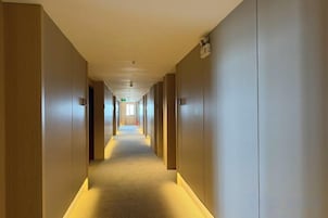 A hotel hallway with doors on both sides, a carpeted floor, and a light-colored ceiling.