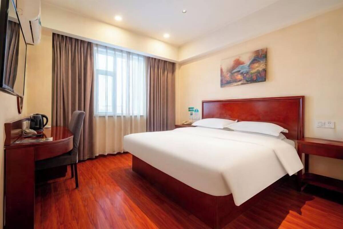 A hotel room with a bed, desk, chair, and a painting on the wall.