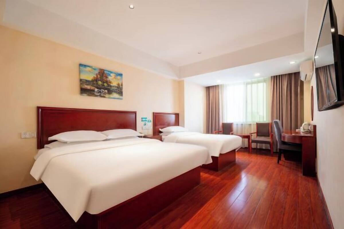 A hotel room with two beds, a desk, a chair, a TV, and a painting on the wall.