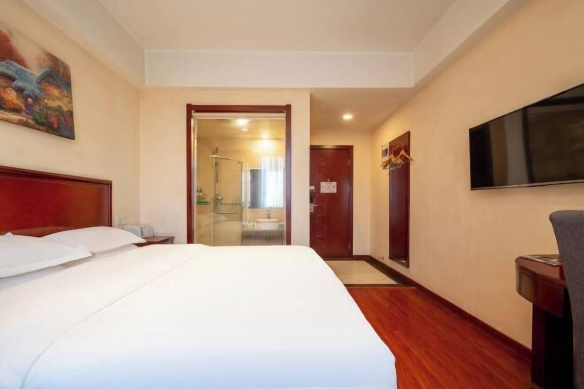 A hotel room with a large bed, a TV, and a shower area visible through a glass door.