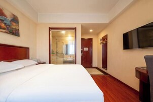 A hotel room with a large bed, a TV, and a shower area visible through a glass door.