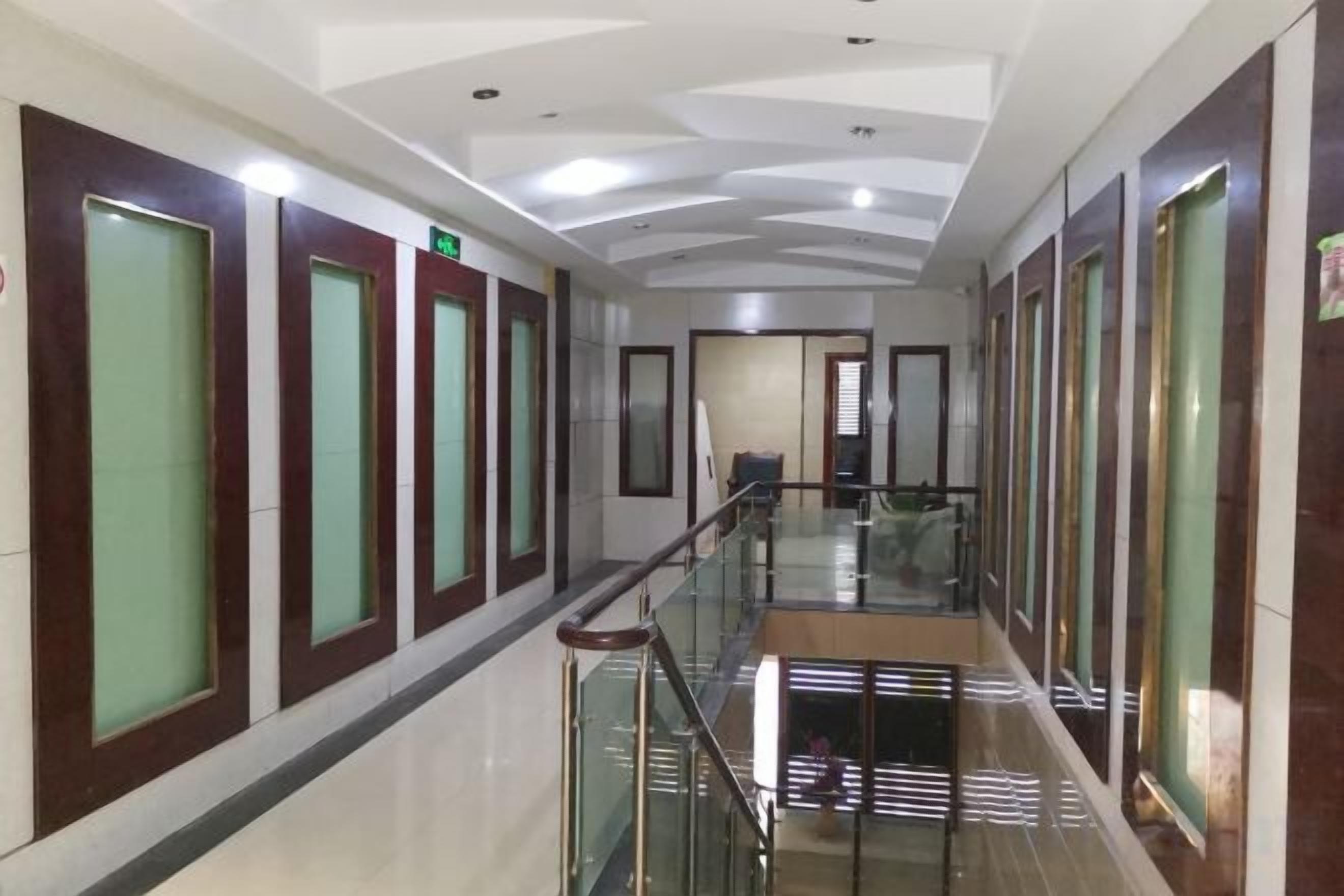 Un pasillo de hotel con barandillas de vidrio, puertas con paneles de vidrio esmerilado e iluminación empotrada en el techo.