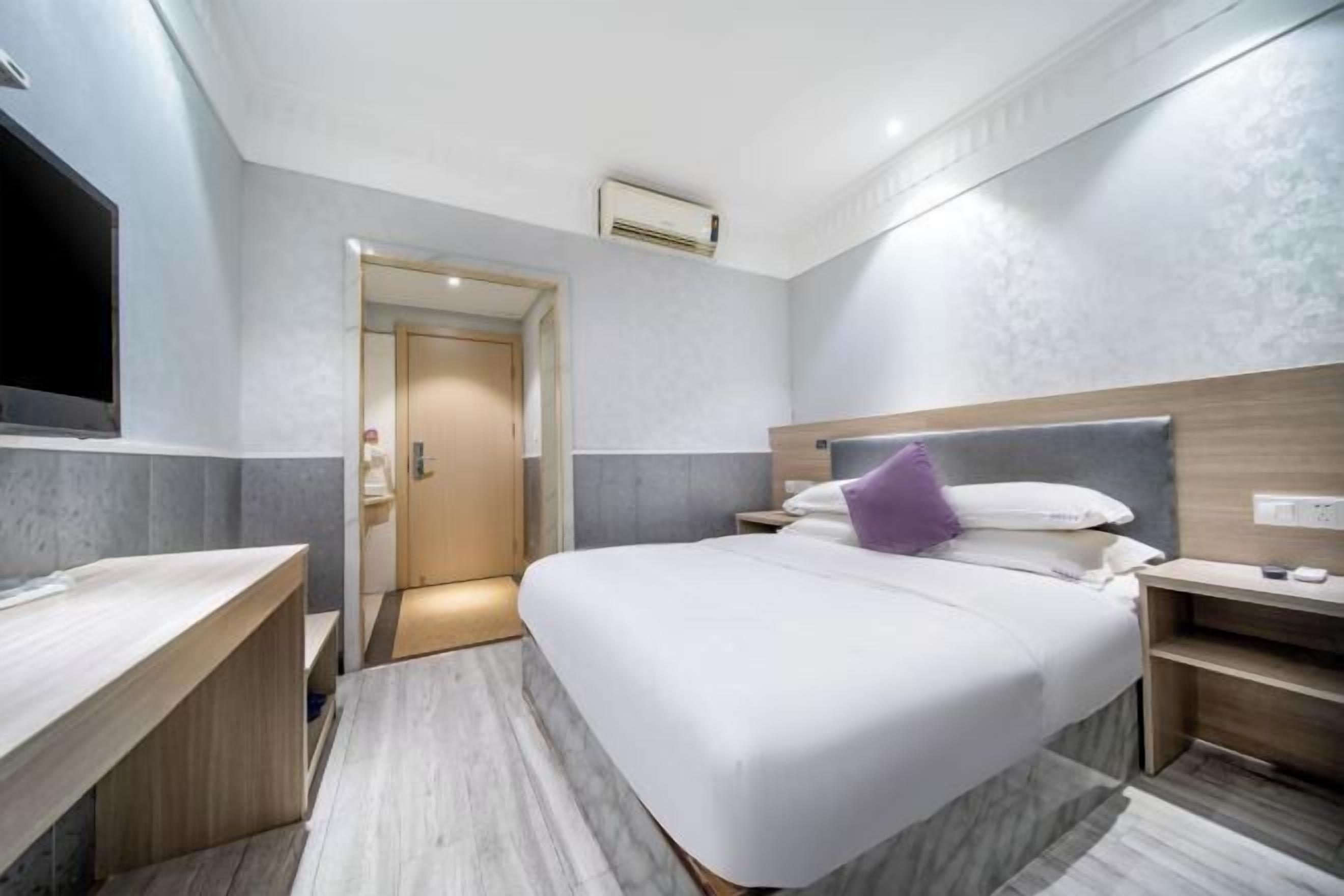 Una habitación de hotel con cama, mesitas de noche, televisor y aire acondicionado.