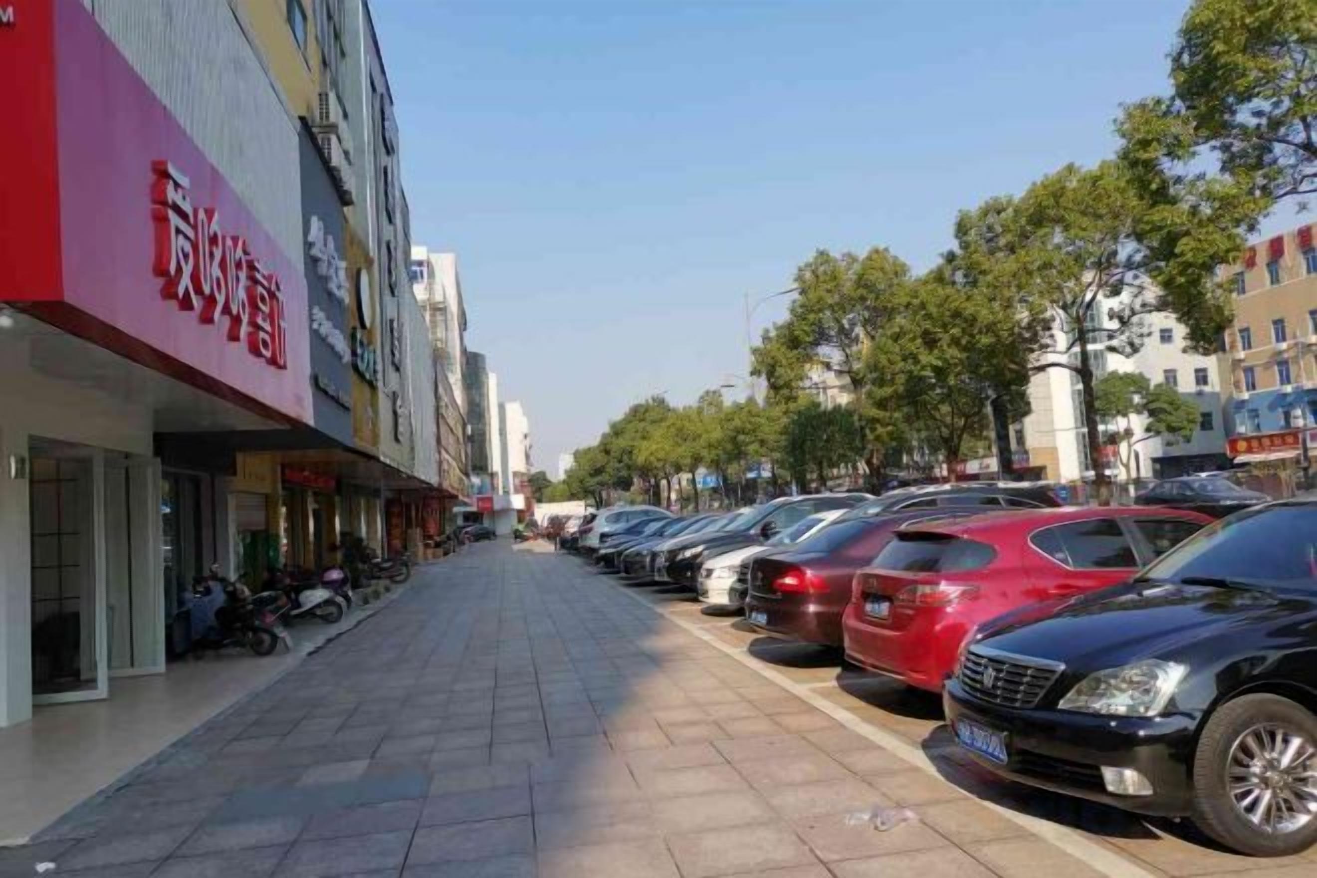 Una calle con coches aparcados y un edificio con toldo rojo.