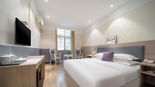 A hotel room with a bed, bedside table, desk, chair, and a TV.