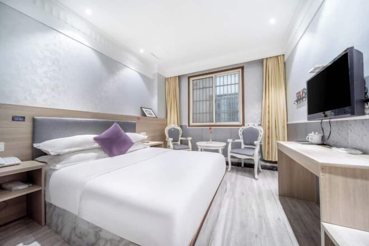 Une chambre d’hôtel avec un lit, un bureau, une chaise, une télévision et une fenêtre.