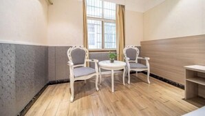 A room with two white chairs, a small round table, a window with curtains, and a wooden floor.