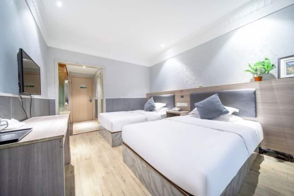 Une chambre d’hôtel avec deux lits, un bureau, un miroir, une plante et une porte donnant sur une autre pièce.