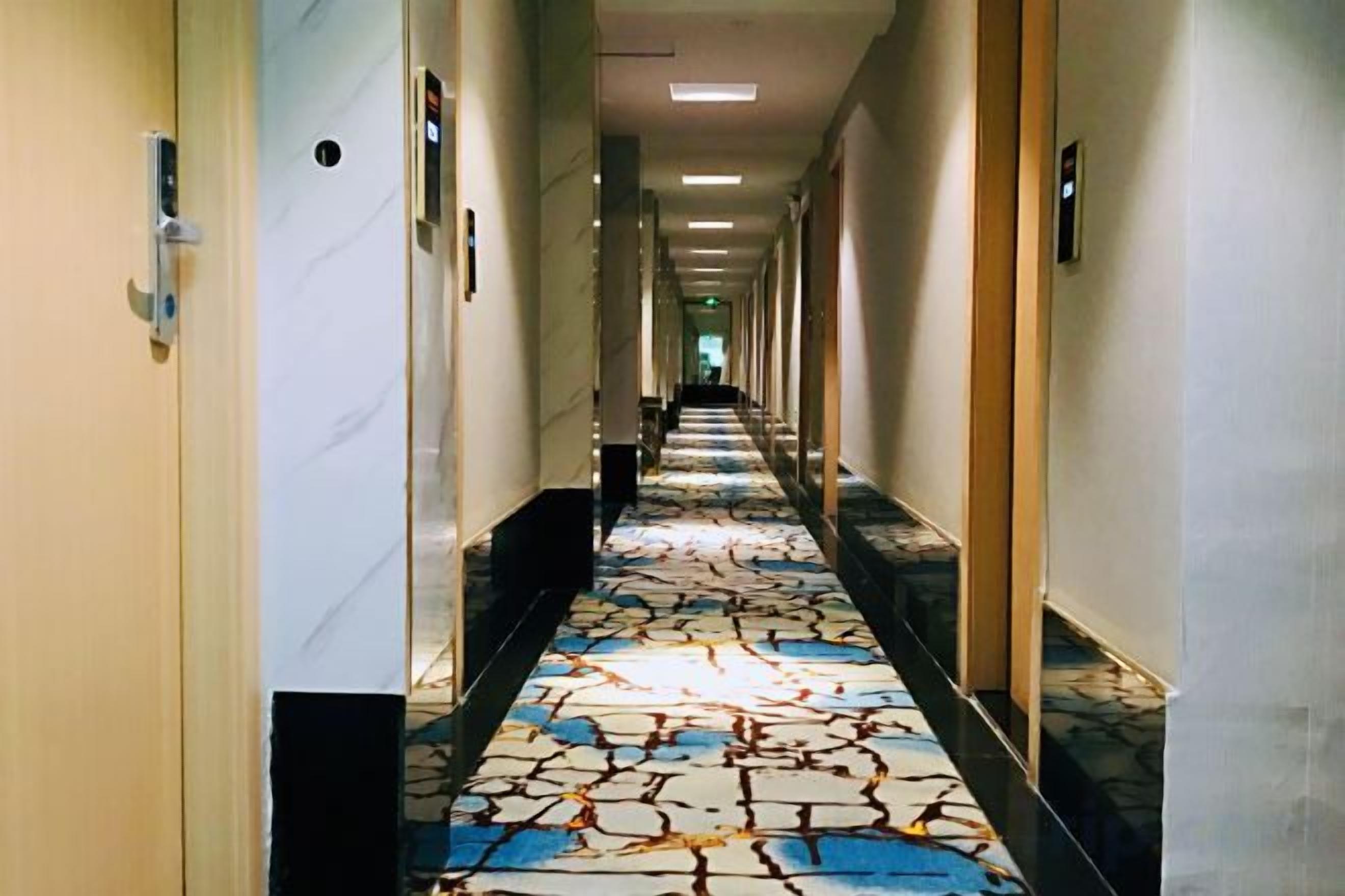 Un pasillo de hotel con alfombra estampada, puertas a ambos lados y un largo recorrido hasta el final.