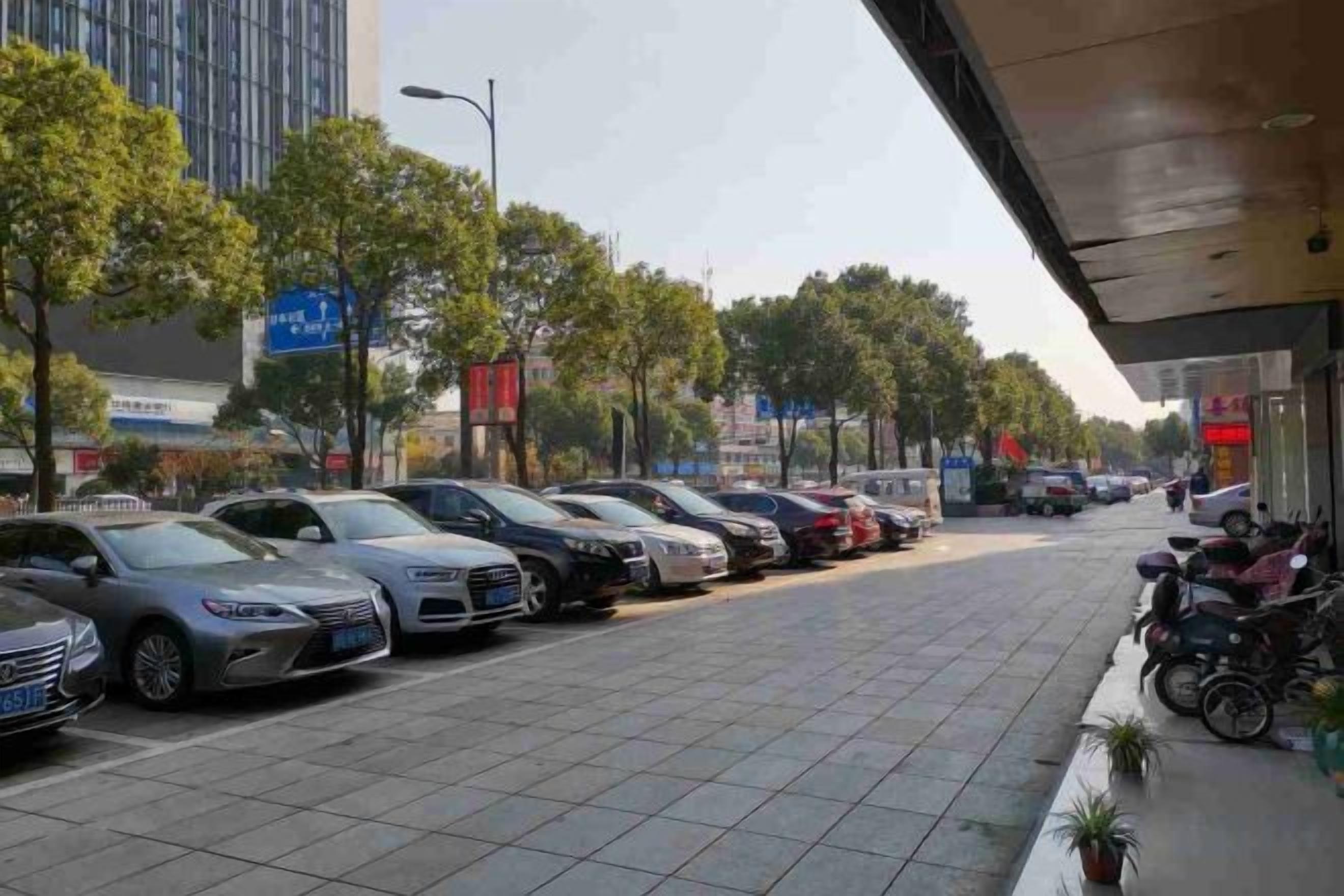 A parking lot with multiple cars and motorcycles, a sidewalk, and a building with signage.