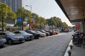 A parking lot with multiple cars and motorcycles, a sidewalk, and a building with signage. - Zijinghua Hotel (Cixi)