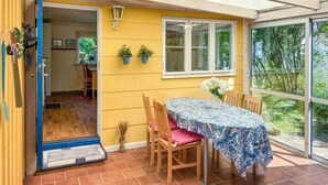 A yellow exterior wall, a window with white blinds, a table with a floral tablecloth, and a door with a blue frame. - 3 bedroom gorgeous home in Halmstad (Halmstad)