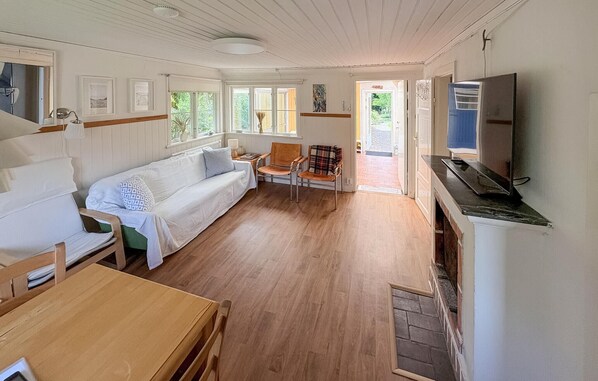 A room with a wooden floor, a sofa, a chair, a table, a TV, and a door leading outside.
