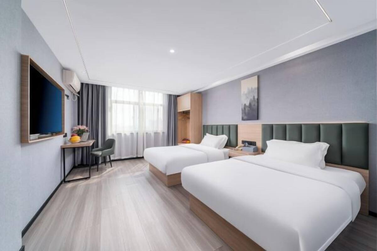 A hotel room with two beds, a desk, a chair, a TV, and a painting on the wall.