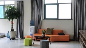 A modern living room with a sofa, ottomans, a coffee table, and a large potted plant. - GreenTree Inn (Taizhou Yangzijiang Middle Road) (Taizhou)