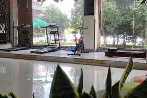A gym with exercise equipment, a window with a view of trees and parked cars, and a tiled floor. - GreenTree Inn (Taizhou Yangzijiang Middle Road) (Taizhou)