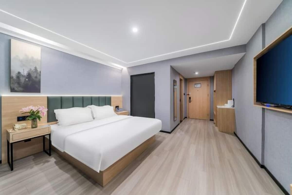 A modern hotel room with a large bed, bedside table, and a flat-screen TV.