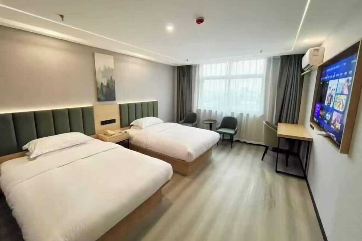 A hotel room with two beds, a desk, a chair, a TV, and a window with curtains.