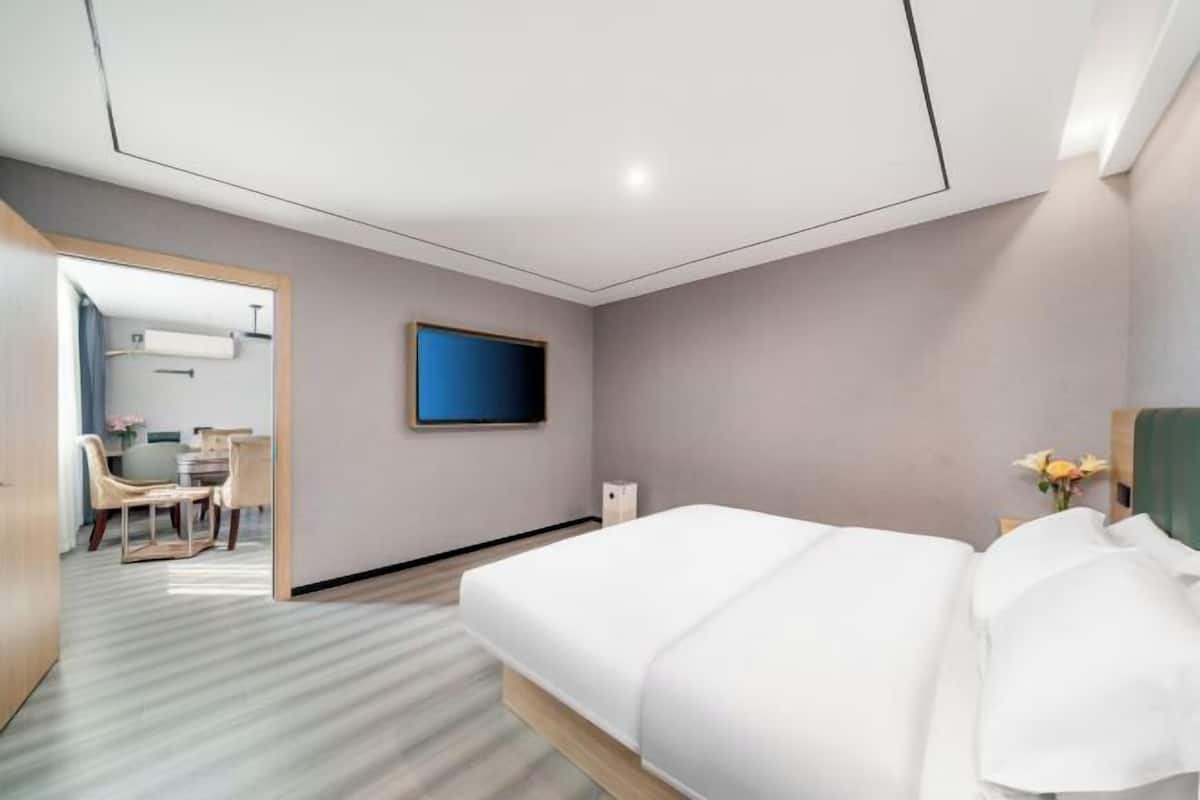 A hotel room with a bed, a television, a desk with chairs, and a view of the hallway.
