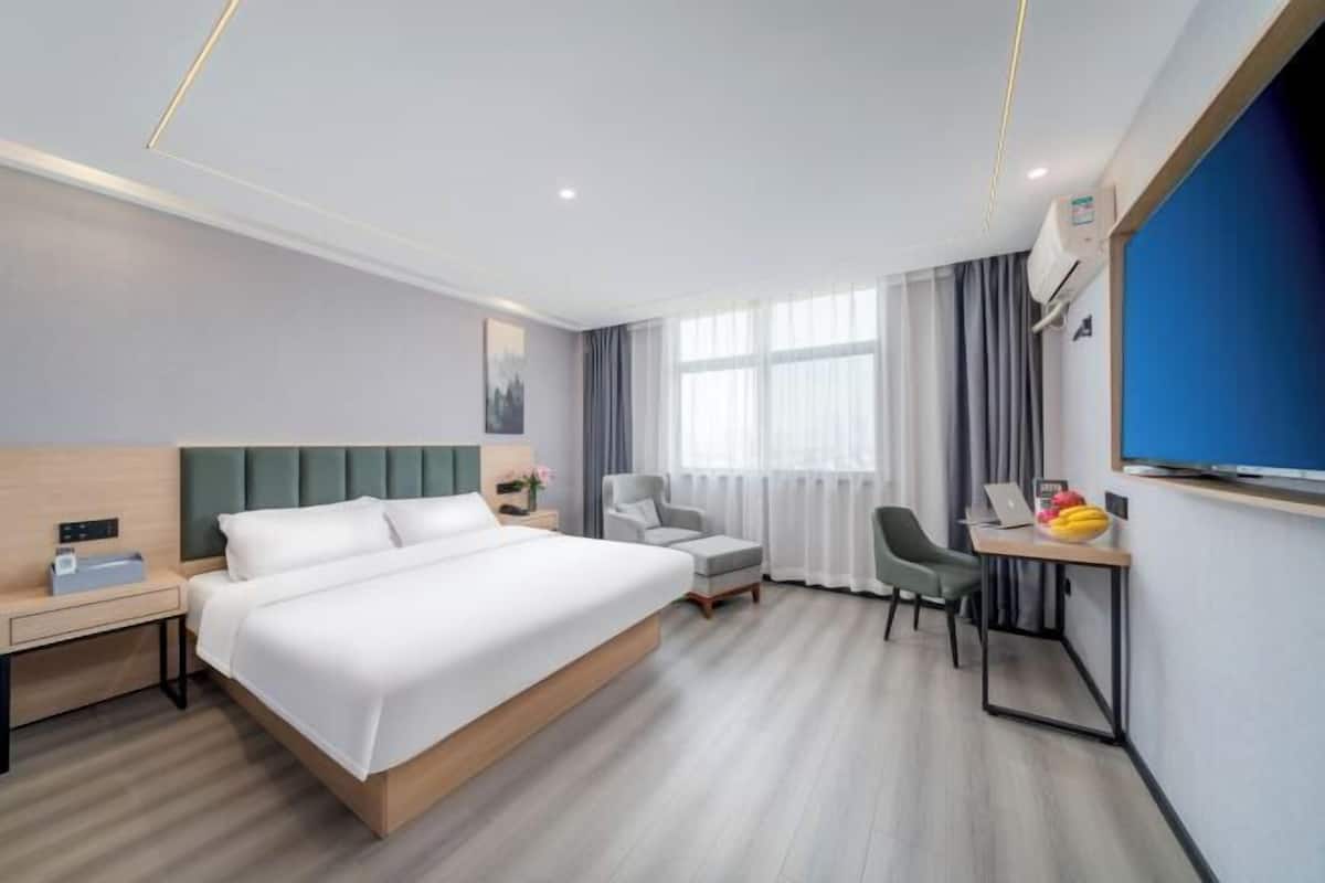A hotel room with a bed, desk, chair, and a TV.