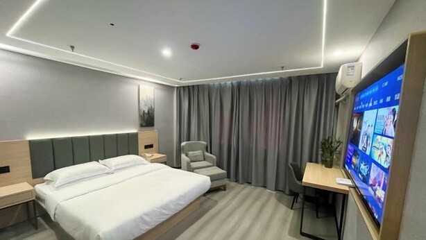 A modern hotel room with a large bed, a desk with a chair, a television, and a grey curtain. - GreenTree Inn (Taizhou Yangzijiang Middle Road) (Taizhou)