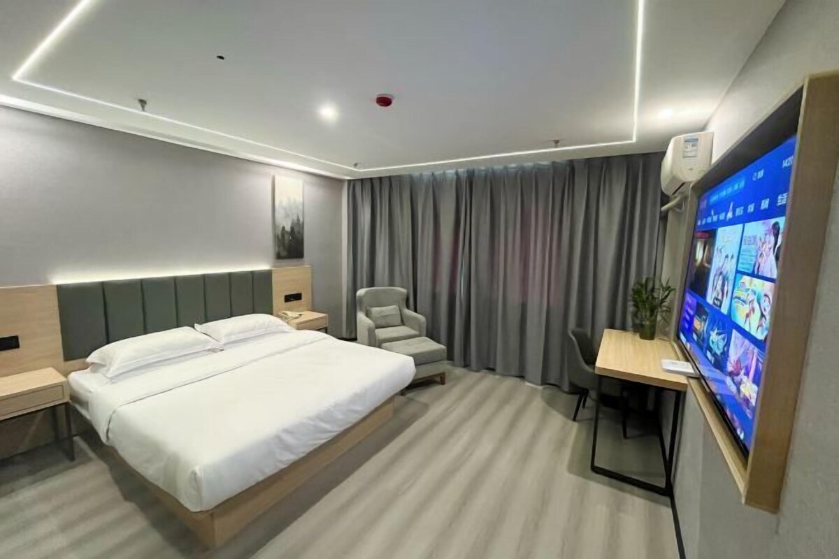 A modern hotel room with a large bed, a desk with a chair, a television, and a grey curtain.