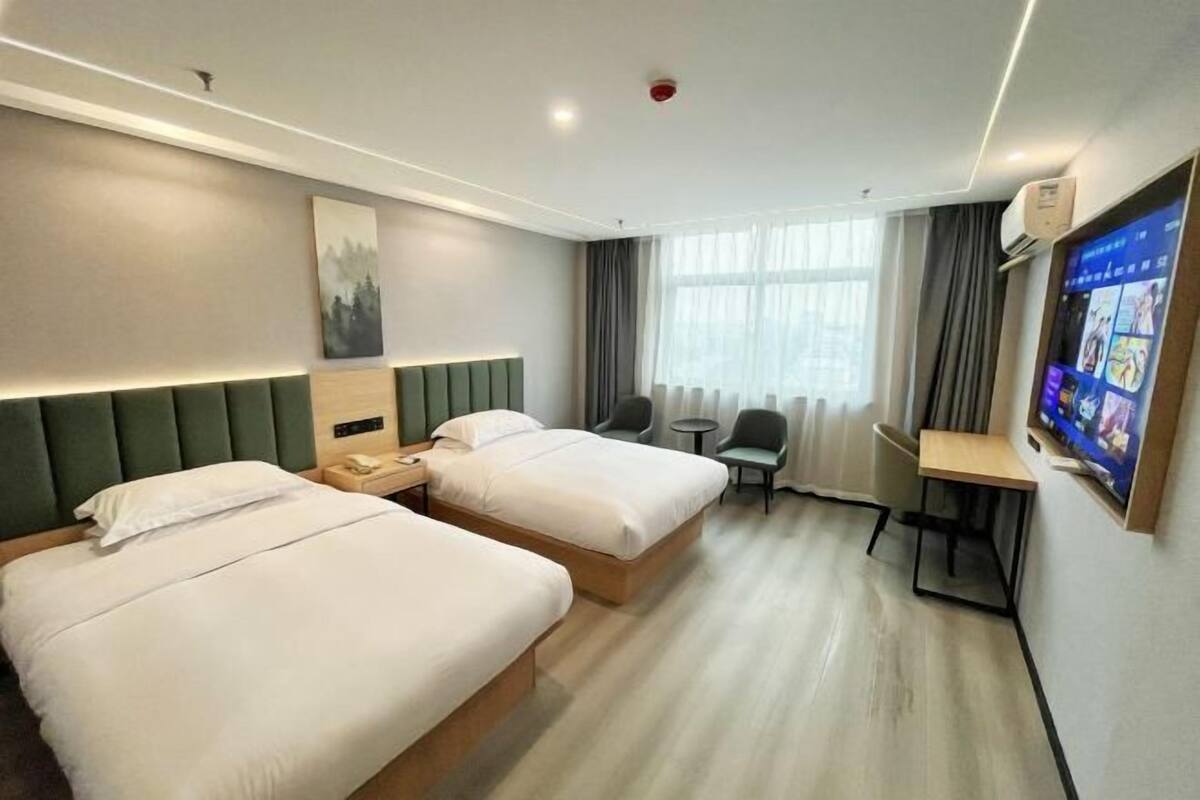 A hotel room with two beds, a desk, a chair, a TV, and a window with curtains.
