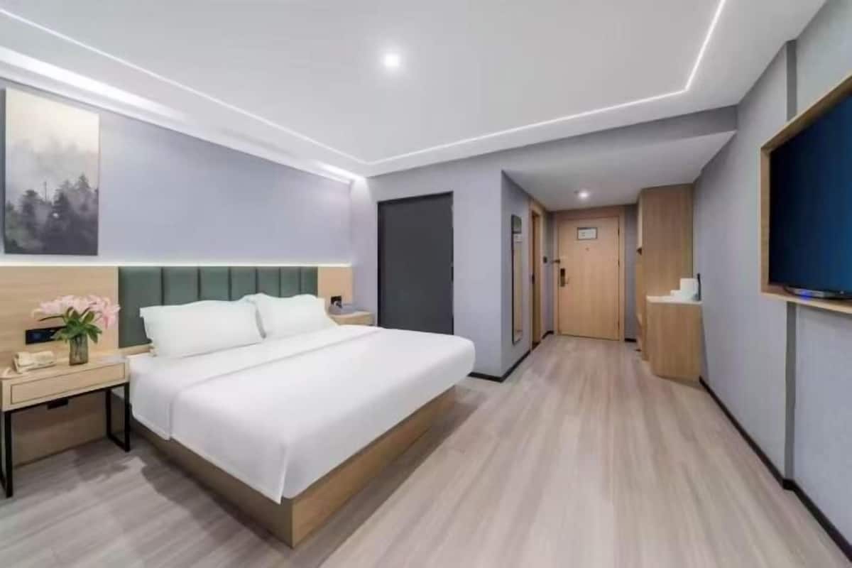 A modern hotel room with a large bed, bedside table, and a television.