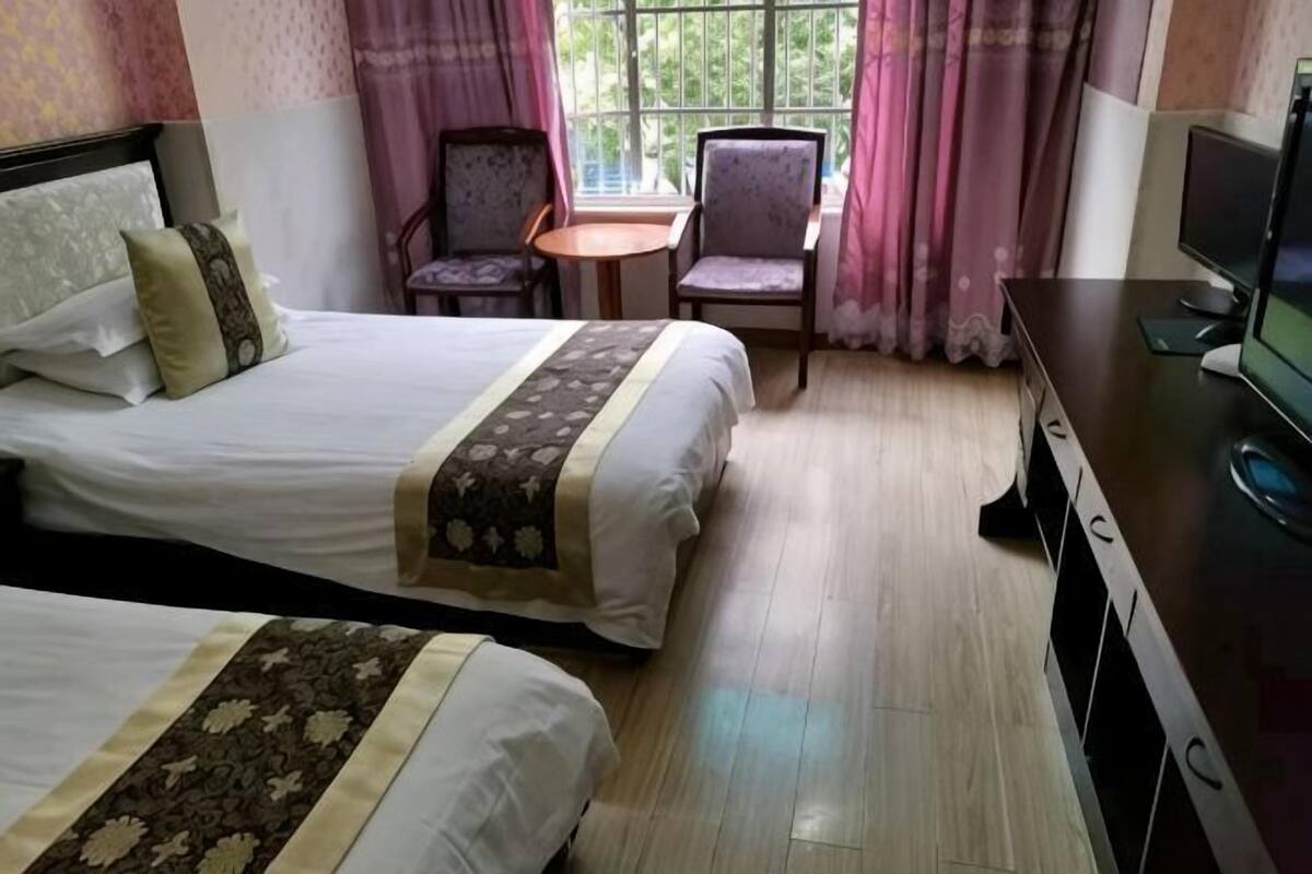 A hotel room with two beds, a desk, a chair, and a television.