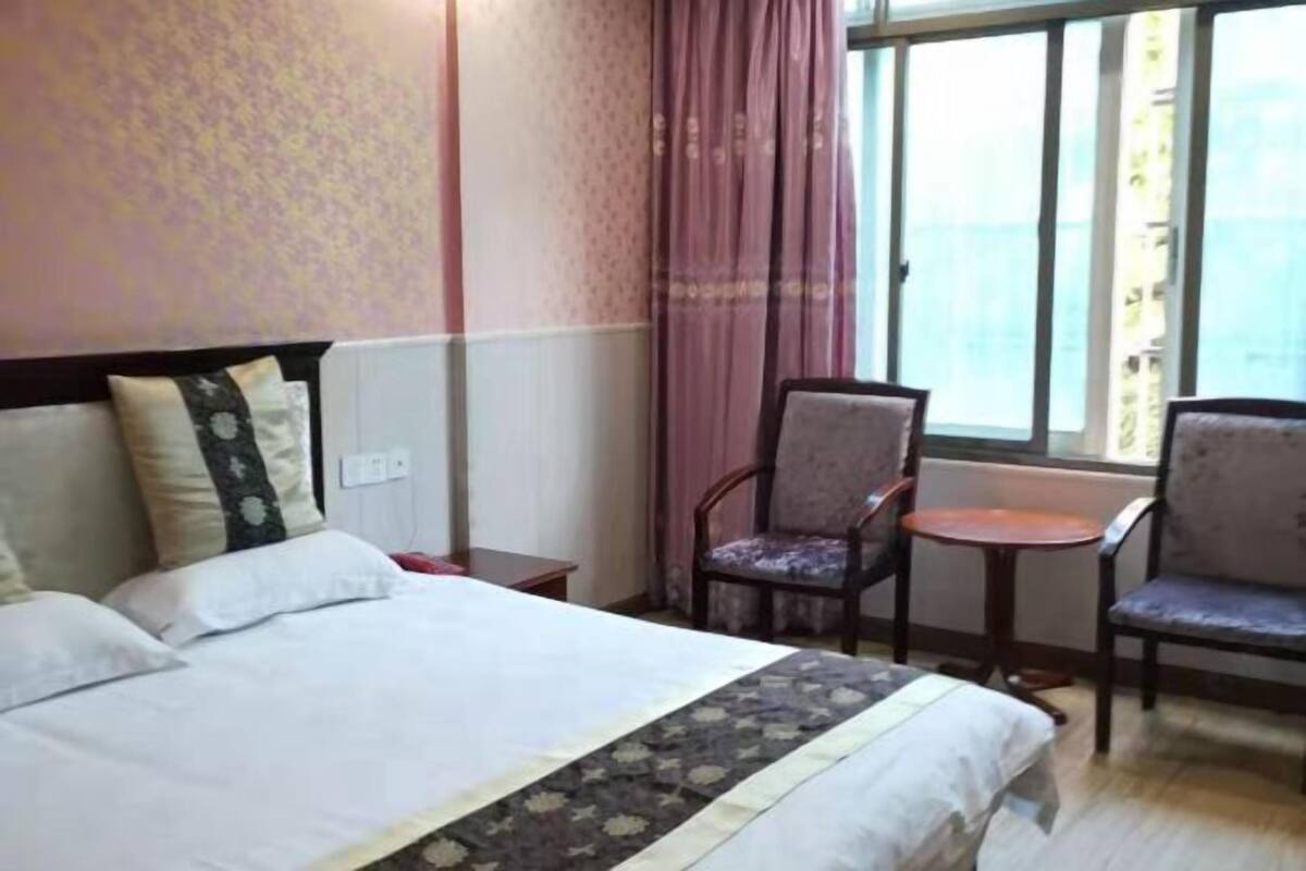 A hotel room with a bed, two chairs, a small table, and a window with curtains.