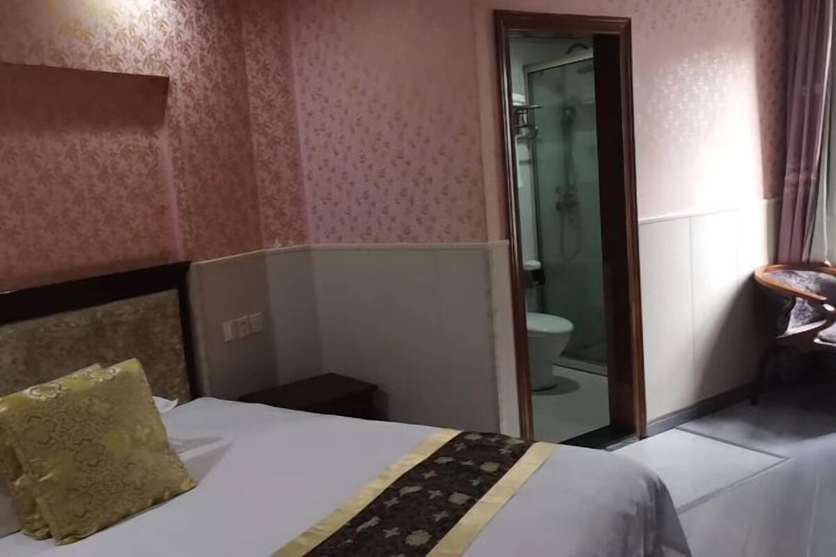 A hotel room with a bed, a small bedside table, a mirror, and a bathroom visible through an open door.