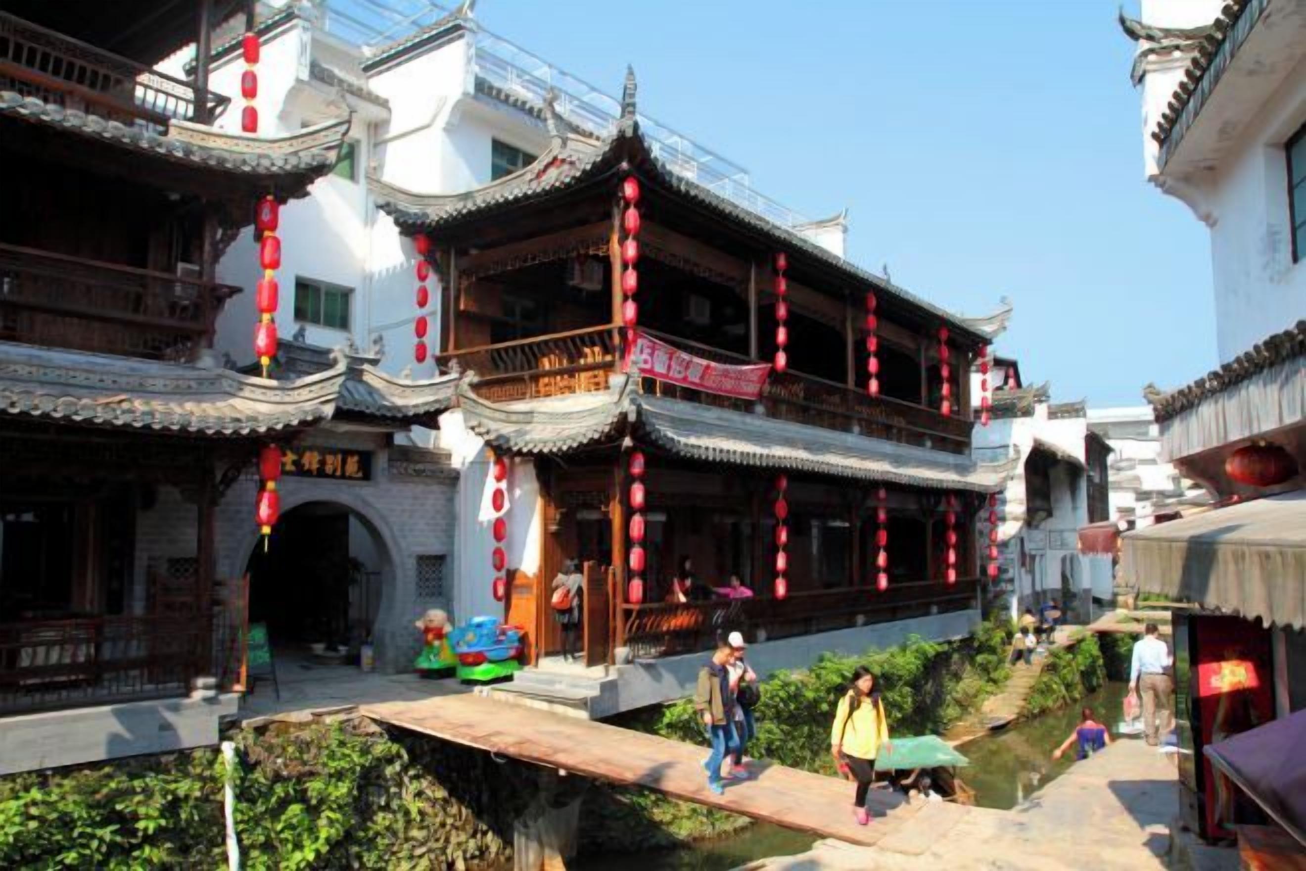 A traditional Chinese courtyard with multi-tiered buildings, a small water feature, and a pedestrian bridge.