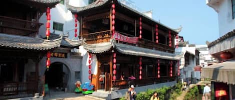 A traditional Chinese courtyard with multi-tiered buildings, a small water feature, and a pedestrian bridge.