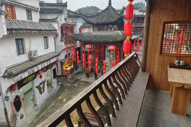 A traditional Chinese courtyard with a wooden balcony railing overlooking a street with red lanterns and traditional architecture.