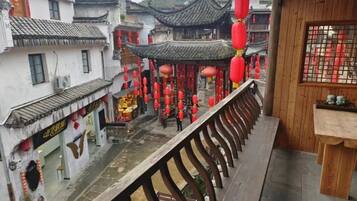 A traditional Chinese courtyard with a wooden balcony railing overlooking a street with red lanterns and traditional architecture.