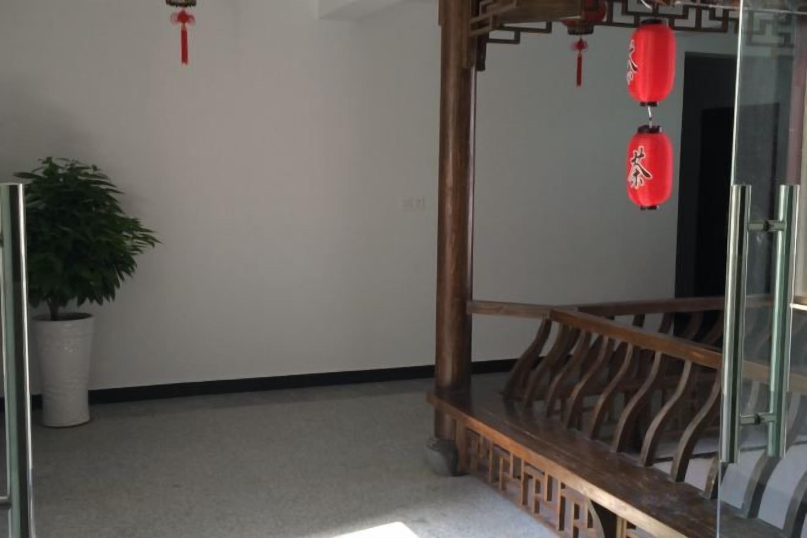 A room with a wooden bench, a potted plant, and red lanterns on the wall.