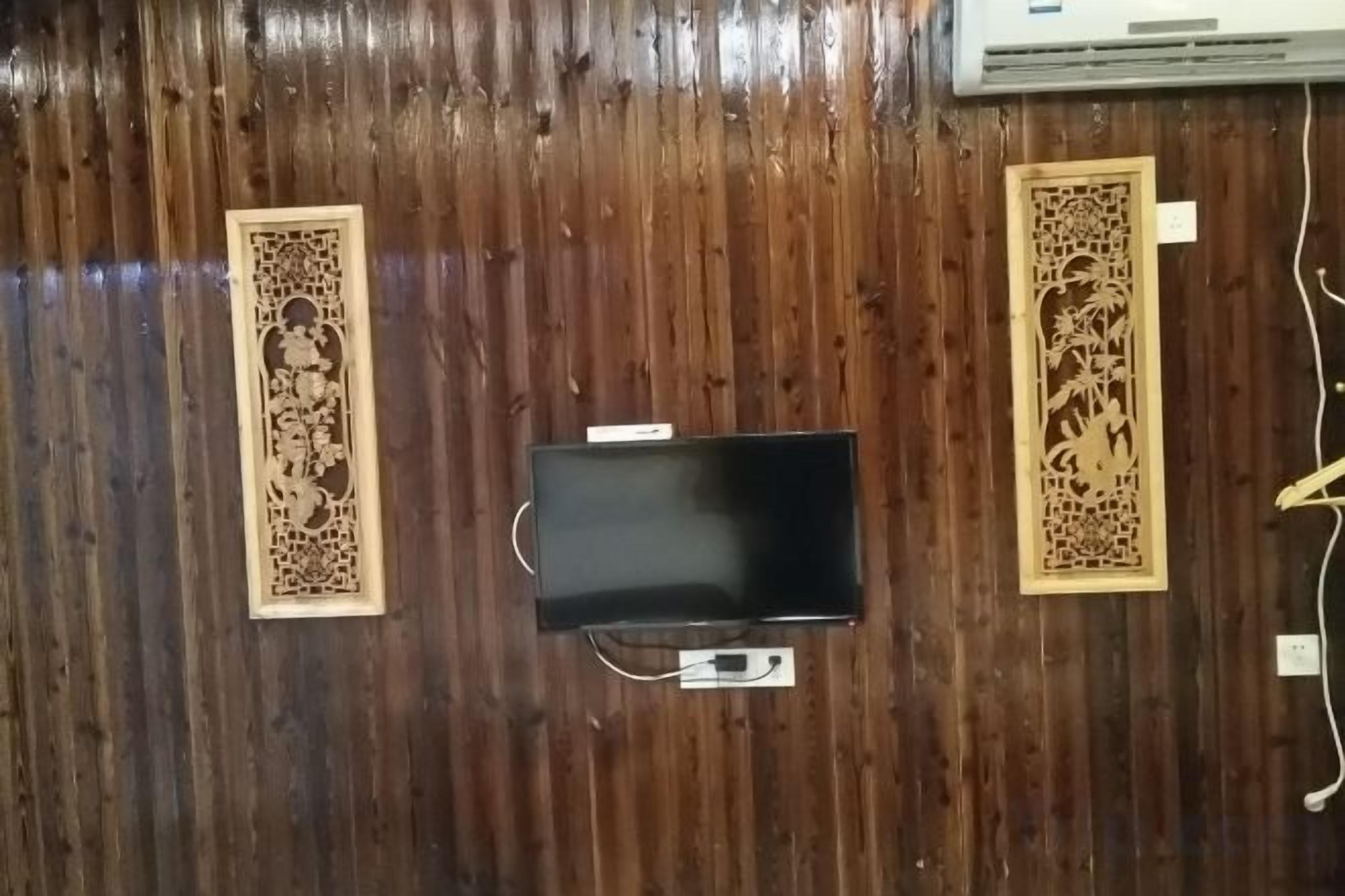 A room with a wooden floor, a flat-screen TV mounted on the wall, and decorative wooden panels on either side.