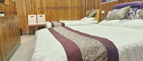 Habitación de hotel con paneles de madera, dos camas con ropa de cama estampada, una ventana con persianas y un aire acondicionado fijado a la pared.