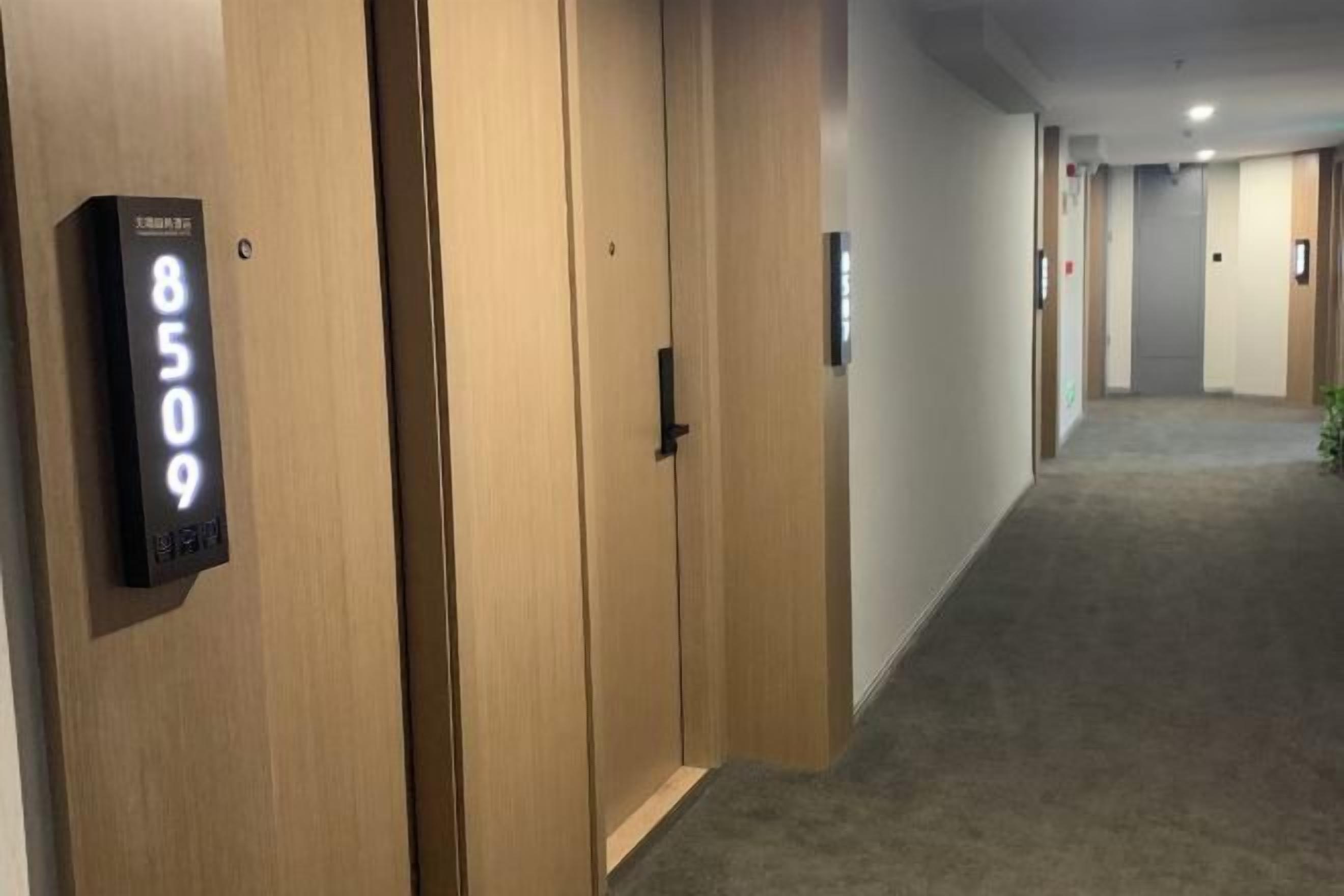 A hotel hallway with wooden doors, a digital number display, and a carpeted floor.