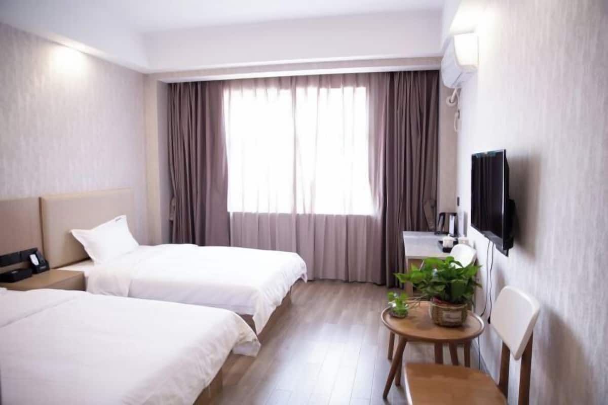 A hotel room with two beds, a desk, a chair, a television, and a window with curtains.